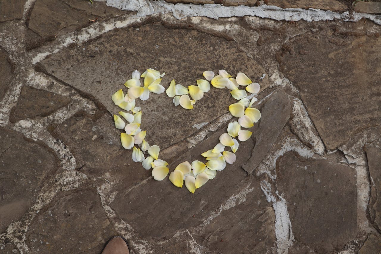 A heart-shaped design of yellow petals arranged on a stone pavement.